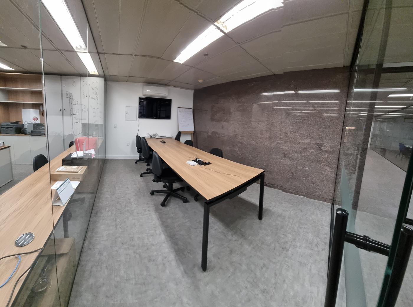 Sala de reunião com divisórias de vidro e mesa para oito pessoas